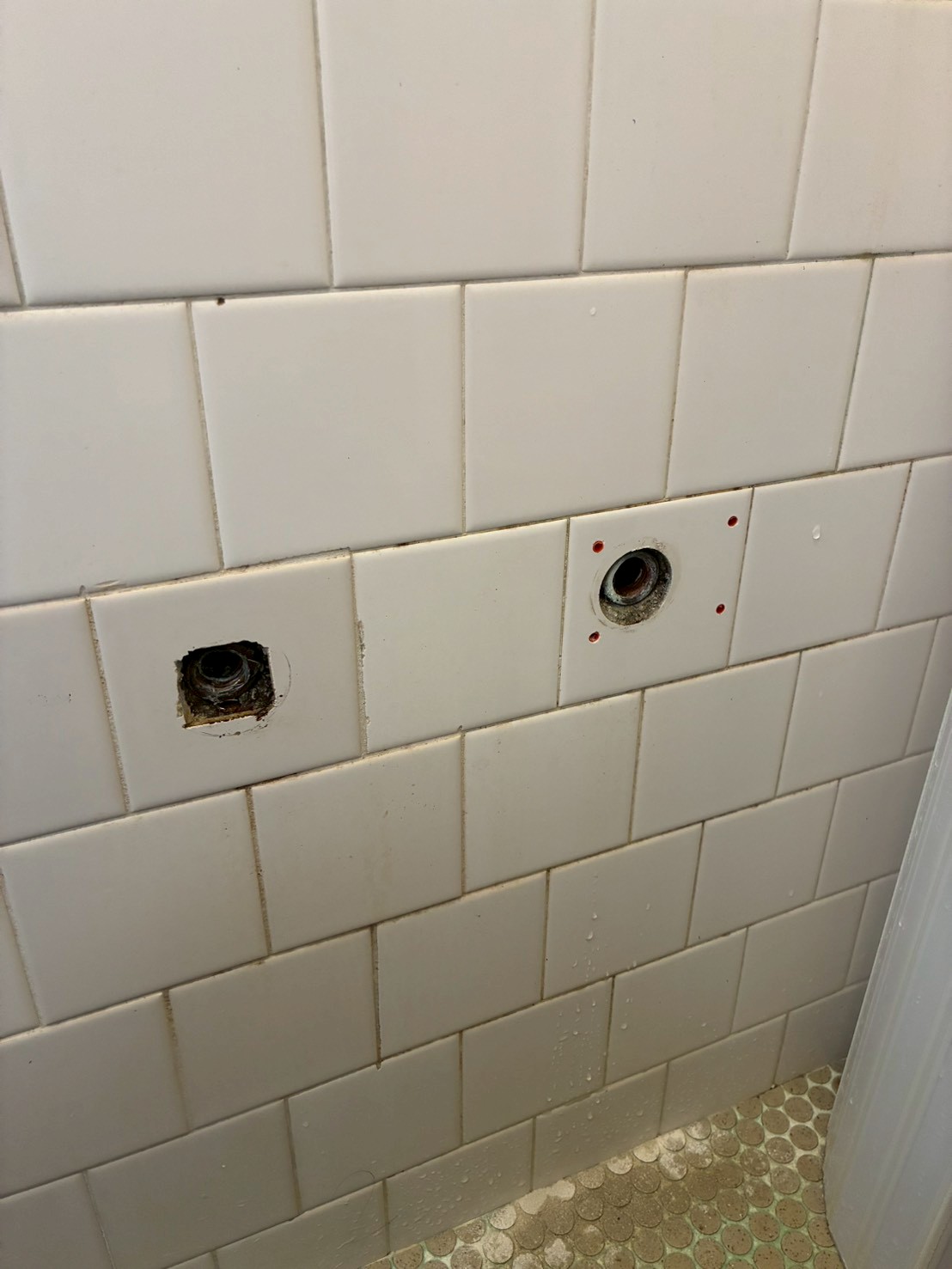 浴室タイルに開いた2つの穴。左は四角く錆びた古いスチール管が見えている